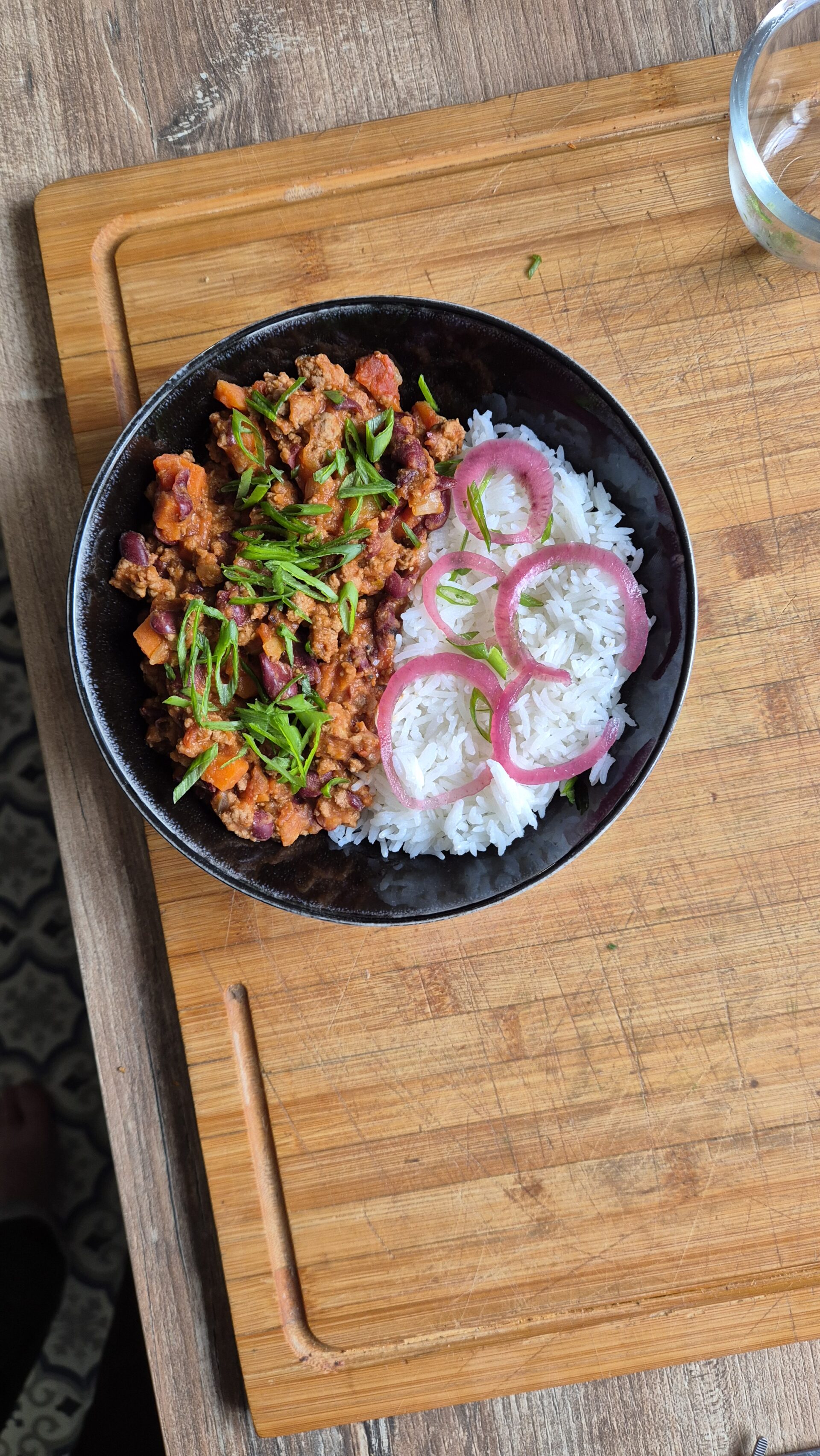 Bol de riz blanc accompagné d’un chili con carne maison, servi chaud avec oignons pickles et herbes fraîches