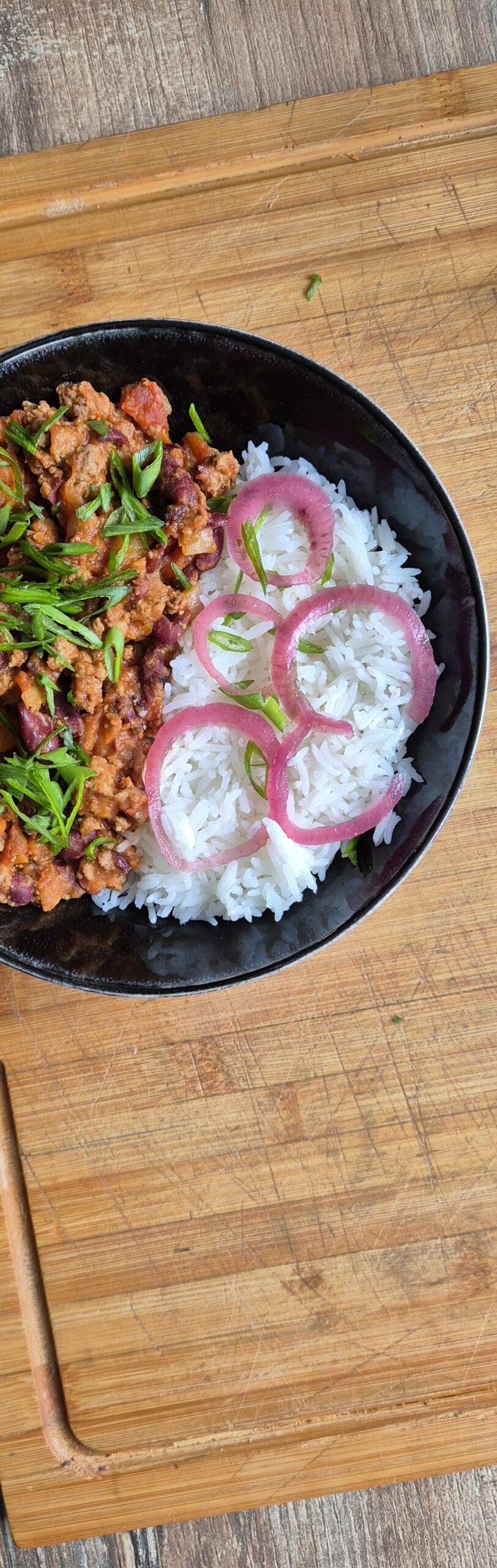 Bol de riz blanc accompagné d’un chili con carne maison, servi chaud avec oignons pickles et herbes fraîches