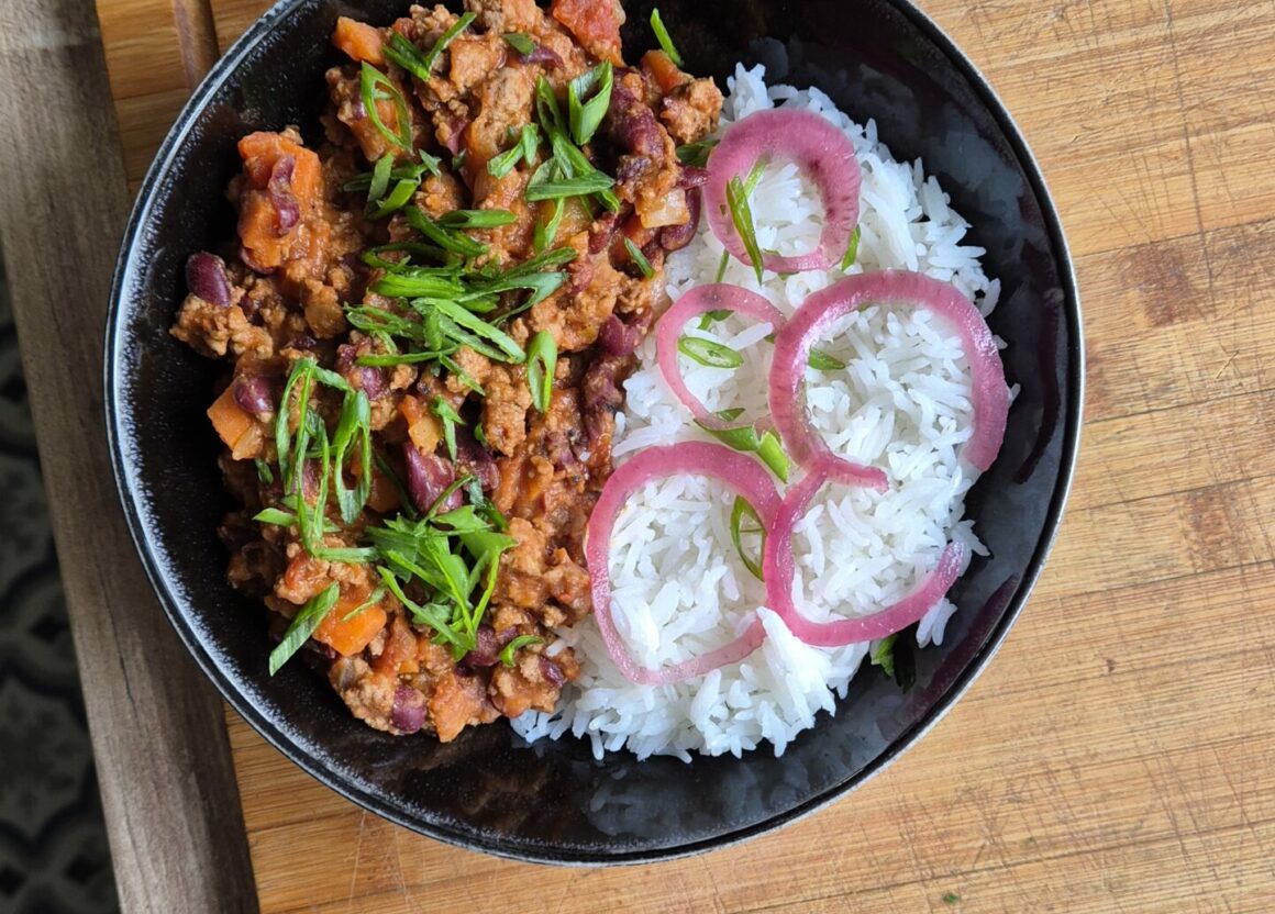 Bol de riz blanc accompagné d’un chili con carne maison, servi chaud avec oignons pickles et herbes fraîches