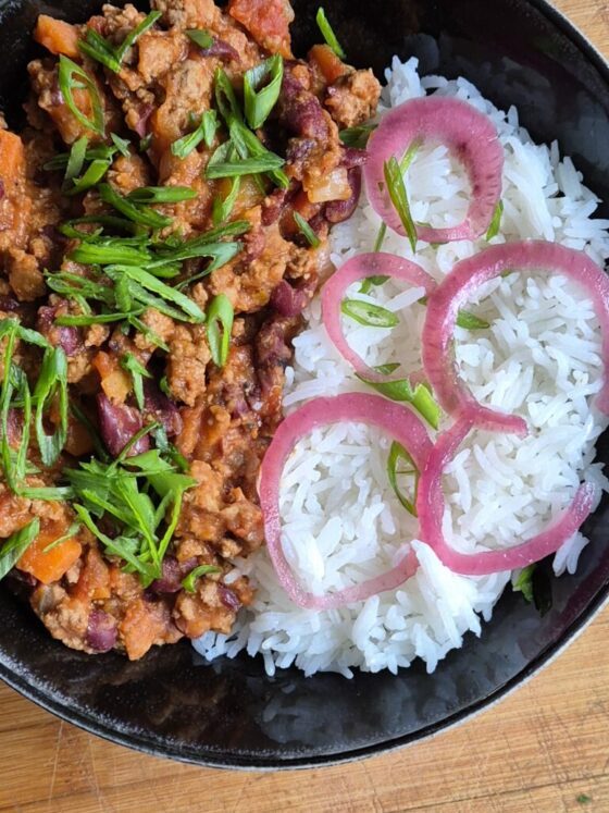 Bol de riz blanc accompagné d’un chili con carne maison, servi chaud avec oignons pickles et herbes fraîches